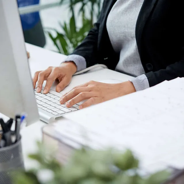 Person skriver på et tastatur på et skrivebord med penner og kontorrekvisita